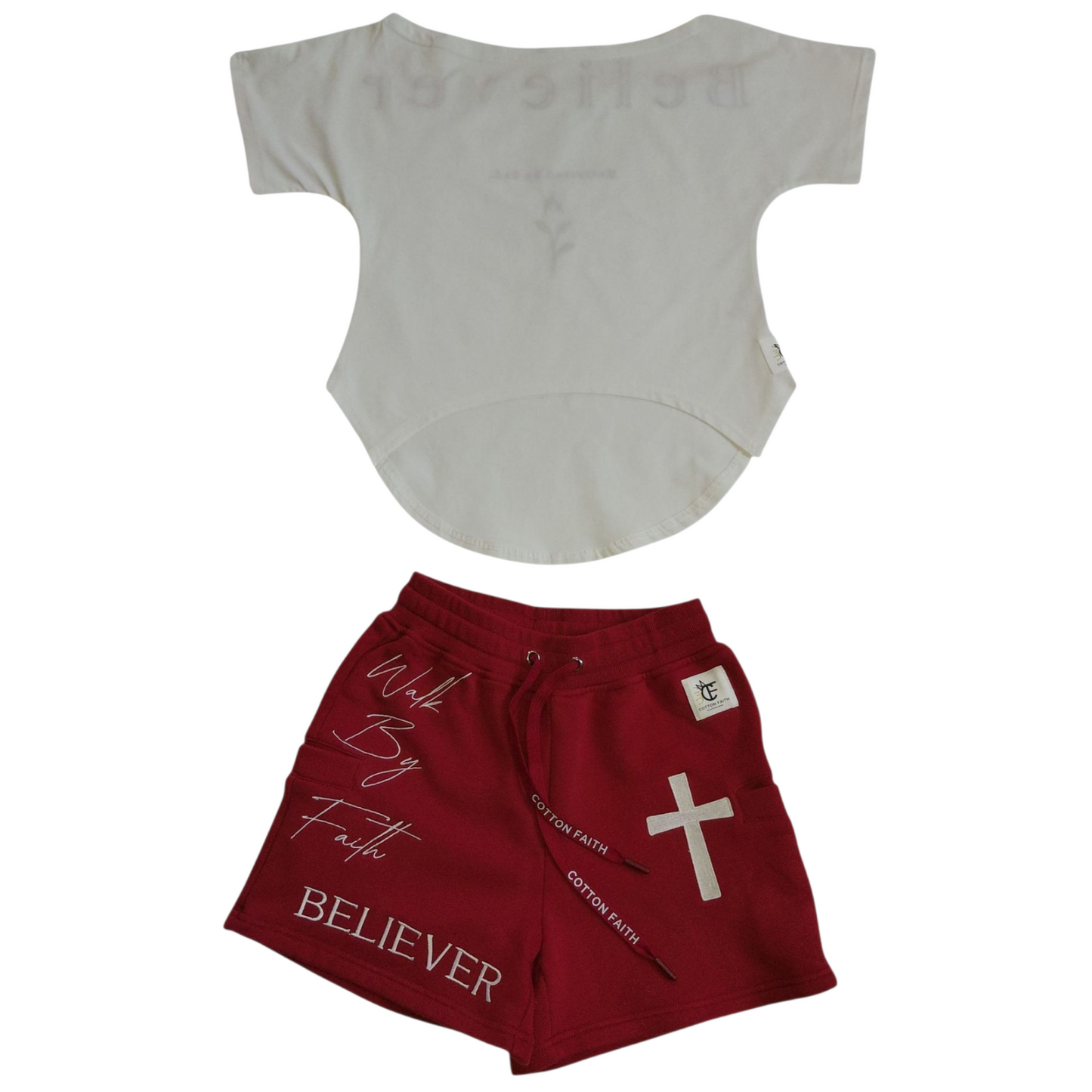 Front of plain white shirt with curved hem, paired with front of red shorts featuring white cross, ‘Walk By Faith’ script, and ‘Believer’ text."
